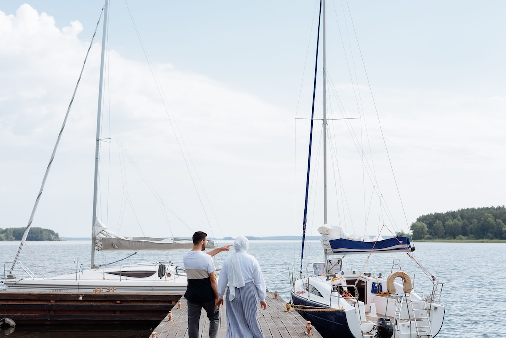 Two people walking along a jetty towards a moored sailboat